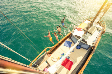 Aerial view of young people jumping from sailing boat on sea trip - Rich happy friends having fun...