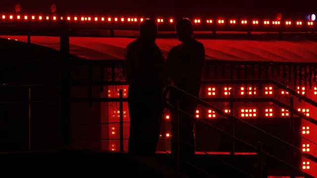 Silhouettes of two unrecognizable men who talk to each other at the entrance to the casino in the late evening.