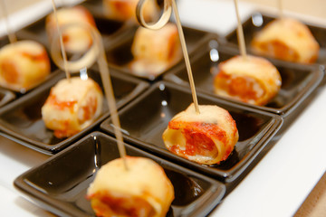 Appetizers made of roasted ham lie in little brown square plates