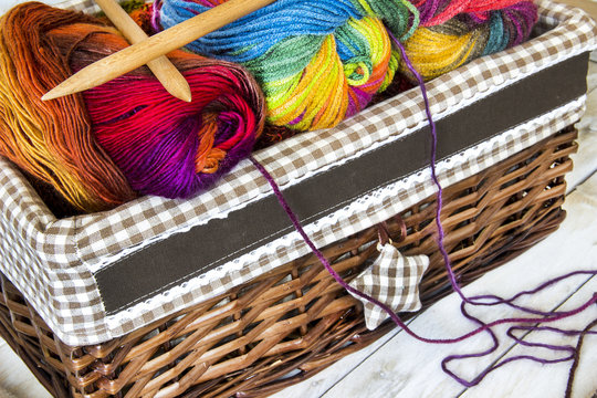 Colorful skeins of wool in knitting basket and needles on wooden background