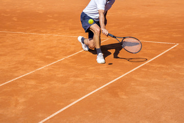 Male tennis player in action on the clay court on a sunny day