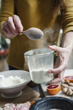 A woman mixing ingredients in a pot, sugar, oranges, petals, and ginger. 
