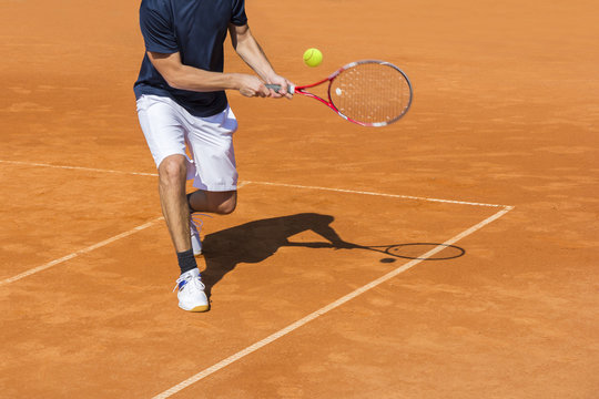 Male tennis player in action on the clay court on a sunny day