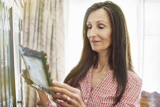 Smiling senior woman with long brown hair holding a picture frame, looking at a picture.
