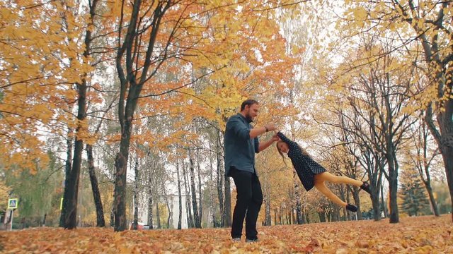 young handsome father turns his cute little daughter around holding her hand in autumn park slow mo