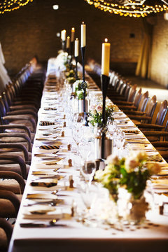 A wedding venue decorated for a party, with fairy lights and a long table set for dinner. 