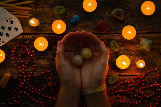 fortuneteller holds crystal balls for divination against a background of candles and runes
