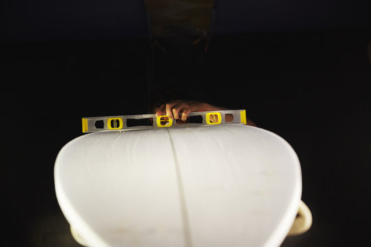 A surfboard in a workshop with a spirit level on the top. 