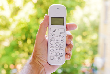 Male hand holding cordless landline telephone receiver outdoors
