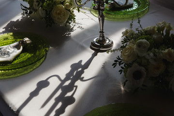 A shadow of silver candleholder lies on the white tablecloth beh
