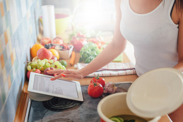 Young woman is preparing a meal while using tablet pc.