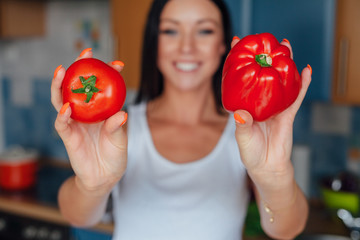 Young woman is holding red peppers in the kitchen.