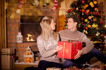 Fototapeta na wymiar Couple in love on the background of New Year and Christmas lights near the burning fireplace consider Christmas gifts