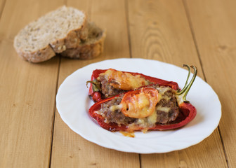 Baked pepper with meat, cheese and tomato on the plate on a wooden table.