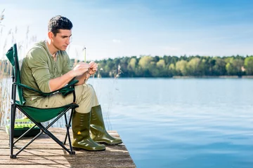 Fototapeten Man fishing at lake fixing lure at angling rod © Kzenon
