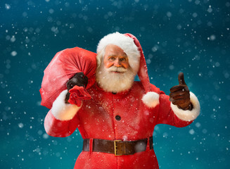Happy Santa Claus gesturing thumb up with big bag full of gifts to children. Merry Christmas & New...