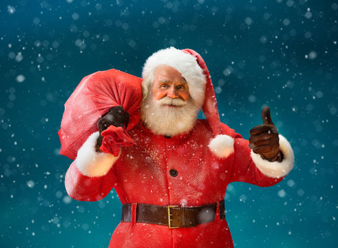 Happy Santa Claus gesturing thumb up with big bag full of gifts to children. Merry Christmas & New Year's Eve concept.