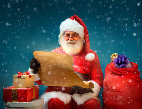 True Santa Claus reads long list of gifts for children on blue background. Merry Christmas & New Year's Eve concept.