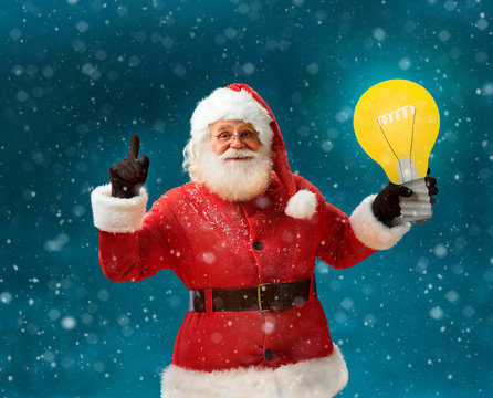 Emotional Santa Claus showing cartoon bulb - having good idea! Smiling Santa Claus on blue background. Merry Christmas & New Year's Eve concept.
