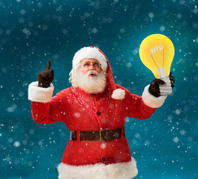 Faddish Santa Claus with open mouth and finger pointing up, showing light bulb banner. Santa Claus on blue background having a good idea. Happy New Year!