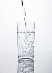 Pouring still clean water in glass on white