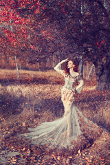 Red hair girl in beautyful fasion dress standing at the yellowed tree