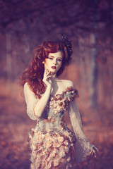 Red hair girl in beautyful fasion dress standing at the yellowed tree