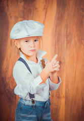 Children's emotions. Artistic little girl in jeans with suspenders, white shirt and a cap on the wooden background