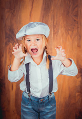 Children's emotions. Artistic little girl in jeans with suspenders, white shirt and a cap on the...