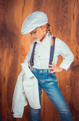 Children's emotions. Artistic little girl in jeans with suspenders, white shirt and a cap on the...