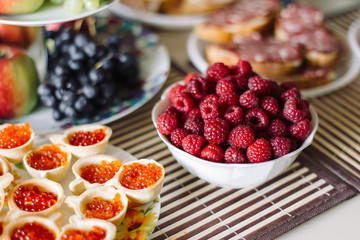 Table with snacks. In the foreground a dish raspberries.