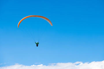 Paraglider gliding over white clouds in clear blue sky