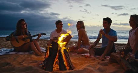 Group of friends relaxing around bonfire on the beach at sunset