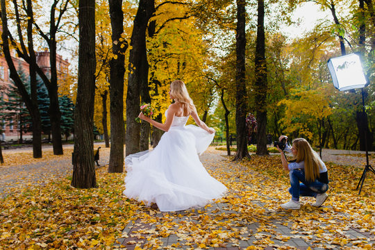Wedding photographer is shooting portrait of the bride in the autumn park