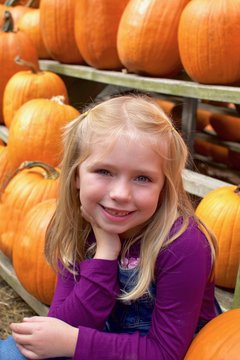 adorable young girl sitting with pumpkins at farm in october fall autumn