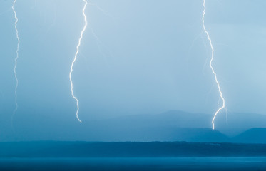 Naklejka na ściany i meble Lightning thunderstorm hitting ground and sea on an island
