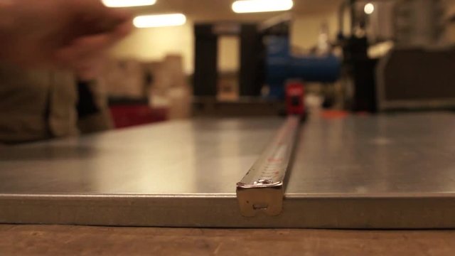 Hand stretches roulette. Measure out the portion of the sheet. The work in the studio. Close-up. Side view. metal sheet lies on Stool. FullHD. It does not contain sound