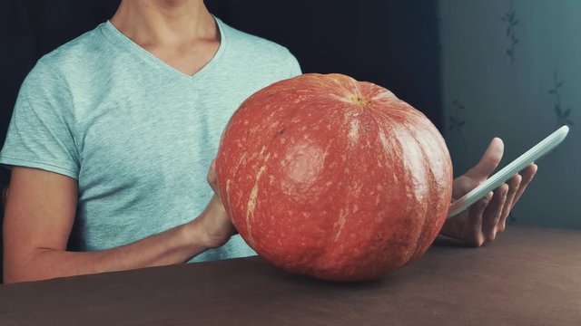 Guy in white shirt use picture on tablet computer as reference and draw on pumpkin jack o lantern 4k