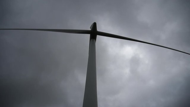 Closeup of a wind turbine spinning against stormy clouds