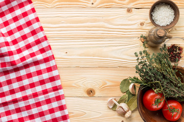 clay plate with tomatoes, herbs, thyme, rosemary, sea salt, olive oil in clay jug, garlic,  pepper, bay leaf on wooden background with red squared tablecloth, top view. Italian food concept