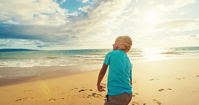 Young boy playing football on the beach at sunset in slow motion