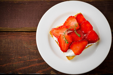 Toasted bread with cream cheese, strawberries and thyme on wooden table