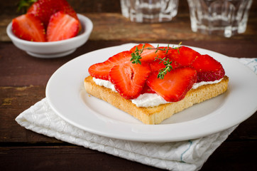 Toasted bread with cream cheese, strawberries and thyme on wooden table