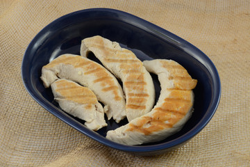 Grilled turkey breast tenderloins in blue bowl on burlap for dinner preparation