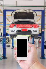 Hand man using smartphone with white screen on blur image of auto repair service as background.