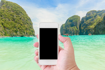 hand using smartphone with black screen front of sunlight on mountain view and sea as background, blue sky as background