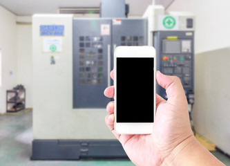 Man use mobile smartphone, blur image of  CNC machining shop with latches as background.