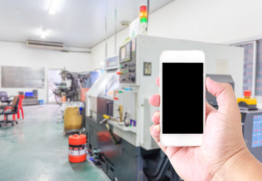 Man use mobile smartphone, blur image of  CNC machining shop with latches as background.
