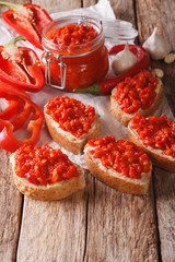 Ajvar in a glass jar and toast on a wooden background. Vertical
