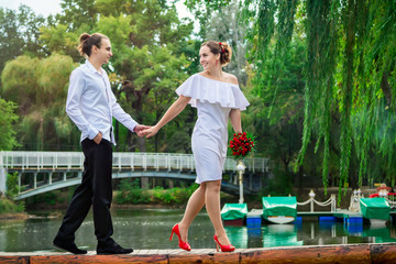 Happy loving wedding couple - beautiful young bride in white dress and groom walking on a wooden bridge over pond in a park